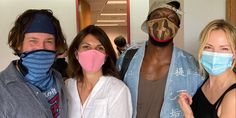 three people with face masks on posing for a photo in front of a group of other people