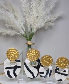 three white and black earrings sitting on top of a table next to a vase filled with flowers