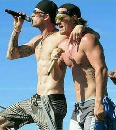 two shirtless men singing into microphones while standing next to each other on stage