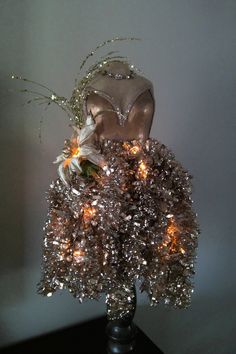 a silver vase filled with lots of lights on top of a black table next to a white wall