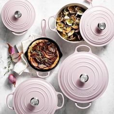 pink pots and pans with clams in them on a white countertop next to an onion dish