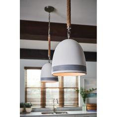 two pendant lights hanging over a kitchen island in front of a window with blinds on the windowsill