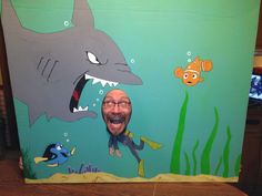 a man standing in front of a painting of a shark and an orange fish with his mouth open