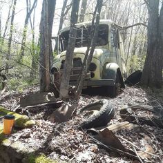 an old bus sitting in the woods surrounded by leaves and branches with tires on it