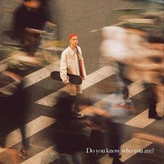 a man holding a skateboard standing in the middle of a crosswalk with people walking by