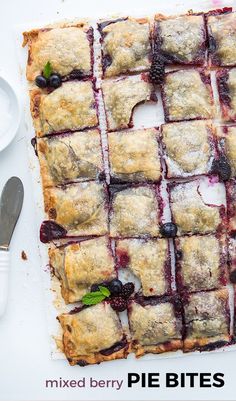 a pie with berries and cream on it sitting next to a fork, knife and spoon