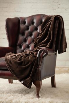 a chair with a blanket on it sitting in front of a brick wall and white rug