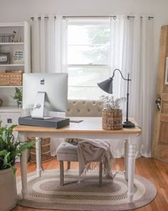 a desk with a computer on top of it next to a potted plant in front of a window