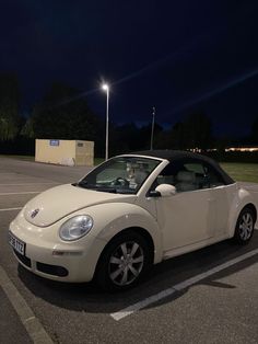 a small white car parked in a parking lot at night with the lights on behind it