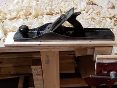 a pair of black shoes sitting on top of a wooden table next to wood shavings