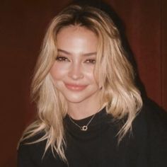 a close up of a person wearing a black shirt and smiling at the camera with long blonde hair