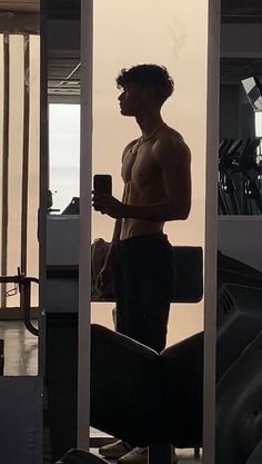 a shirtless man holding a cell phone while standing in front of a gym machine