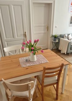 a wooden table topped with a white vase filled with pink flowers on top of a hard wood floor