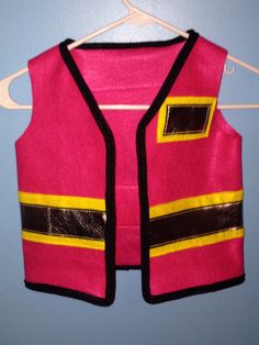 a pink and yellow vest hanging on a hanger next to a blue wall,