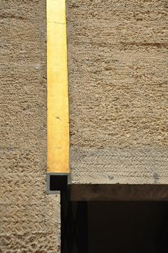 a black and white cat sitting on the side of a building next to a yellow pole