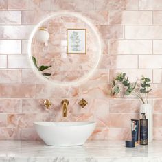 a bathroom with pink marble walls and white counter top, gold faucet sink and round mirror