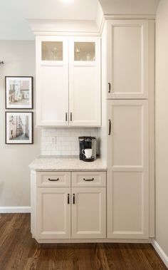 a kitchen with white cabinets and wood flooring in the middle of it, along with pictures on the wall