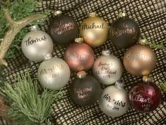 christmas ornaments with names on them sitting next to a pine branch and plaid cloth background