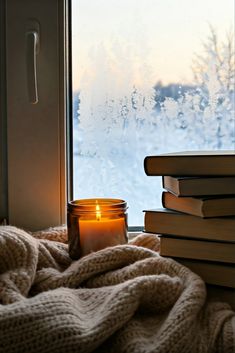 a candle sitting on top of a pile of books next to a window