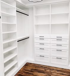 an empty walk in closet with white shelving and wood flooring on the side