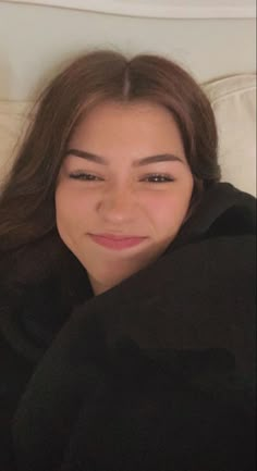 a woman laying on top of a white bed next to a black pillow with her eyes closed