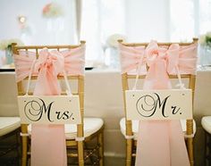 two chairs decorated with pink bows and mr and mrs signs for the bride and groom