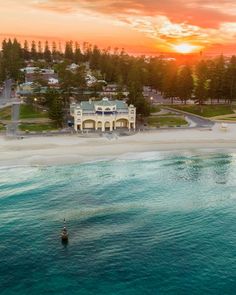 an aerial view of the beach and ocean at sunset, with houses in the background