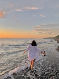 a woman walking on the beach at sunset with her arms spread out to the water