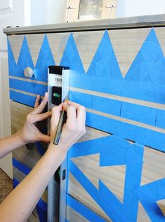 a person is using tape to paint the side of a cabinet