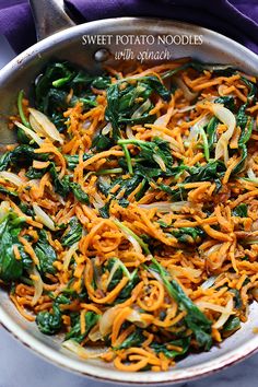 a pan filled with noodles and spinach on top of a purple cloth next to a spoon