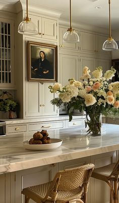 a kitchen with white cabinets and flowers in the vase on the counter top, along with two bar stools