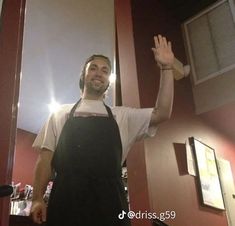 a man in an apron waves to the camera