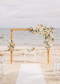 an outdoor wedding setup on the beach with white flowers and greenery at the end of the aisle