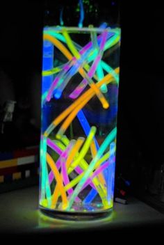 a glass filled with neon colored sticks on top of a table