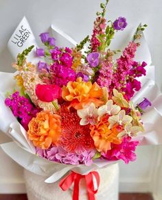 a bouquet of colorful flowers in a white vase with red ribbon on the top and bottom