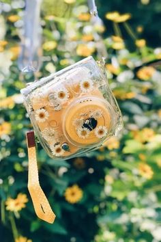 a camera hanging from a string in front of some yellow and white flowered bushes