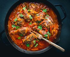 a skillet filled with meat and vegetables on top of a black table next to a wooden spoon