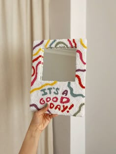 someone is holding up a small mirror decorated with colorful designs and writing on the frame