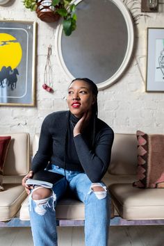 a woman sitting on top of a couch in front of a wall with pictures and plants