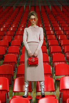 a woman standing in front of red chairs with her hand on her hip, wearing knee high boots