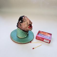 a ceramic head sitting on top of a green plate next to matches