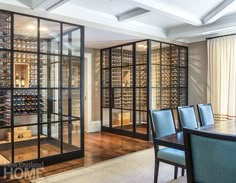 a dining room table and chairs with wine bottles on the wall behind them in a glass case