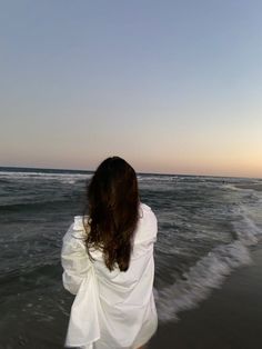 a woman standing in the ocean at sunset with her back to the camera, looking out into the water