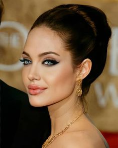 a woman with blue eyes and gold jewelry on her neck is posing for the camera