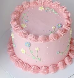 a pink frosted cake with flowers and swirls on it's side, sitting on a white plate