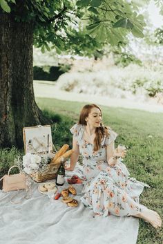 a woman sitting under a tree with food and wine in her hand, on a blanket