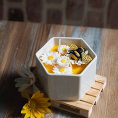 a small white bowl filled with honey and daisies on top of a wooden table