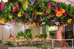 a banquet hall with tables and chairs covered in colorful flowers, greenery and hanging lights