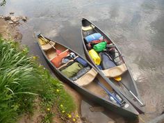 two canoes are sitting on the bank of a river with their oars open