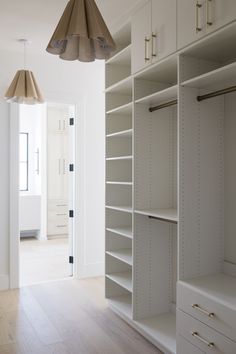 an empty walk in closet with white shelving and hanging lamps above it, along with wooden flooring